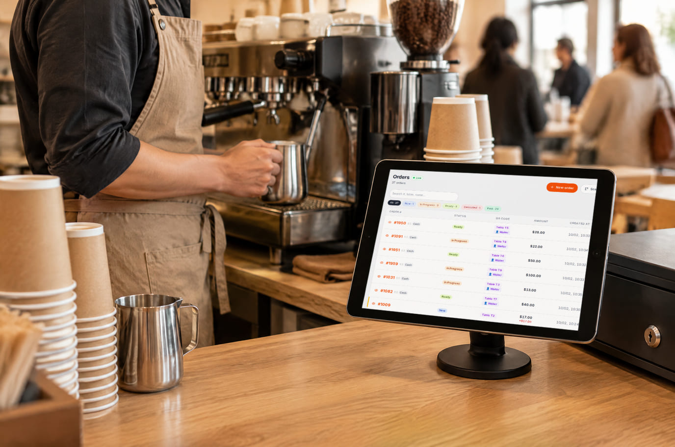 A barista prepares a drink next to a counter tablet showing guest orders from the floor