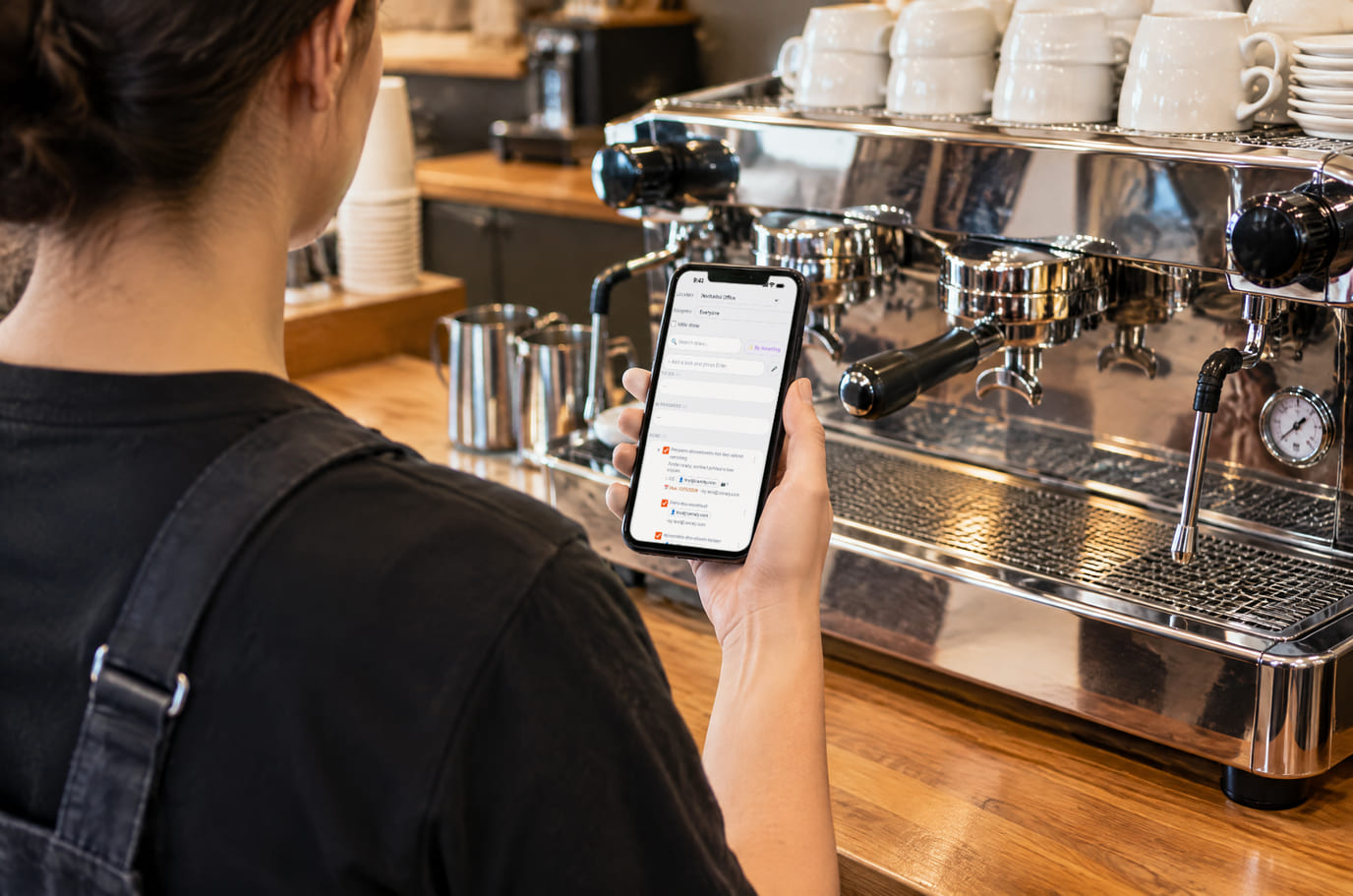 Barista by a cleaned espresso machine closing a task on the phone that requires a photo