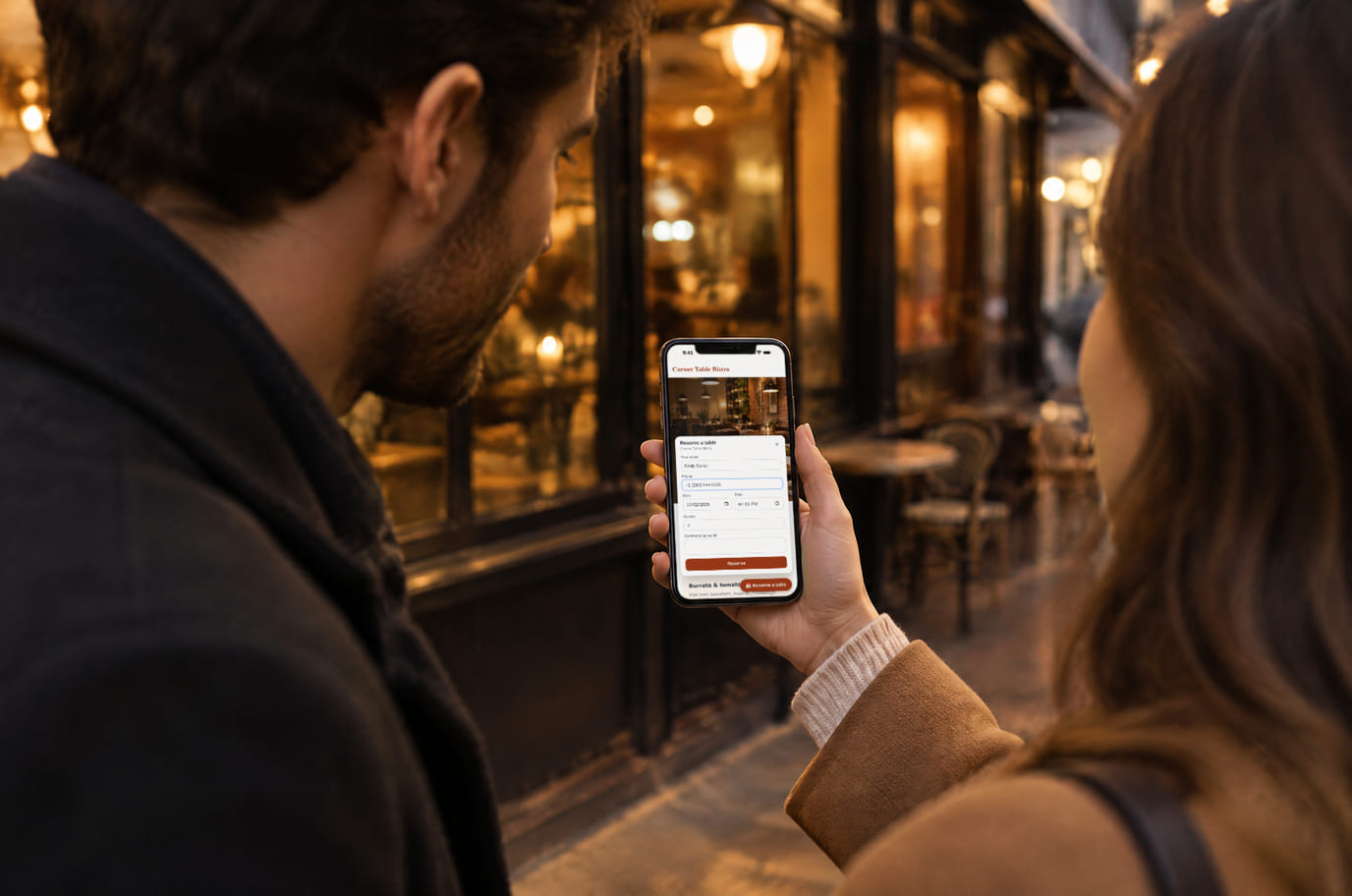 A couple outside a bistro in the evening books a table on a phone through the booking form on its website