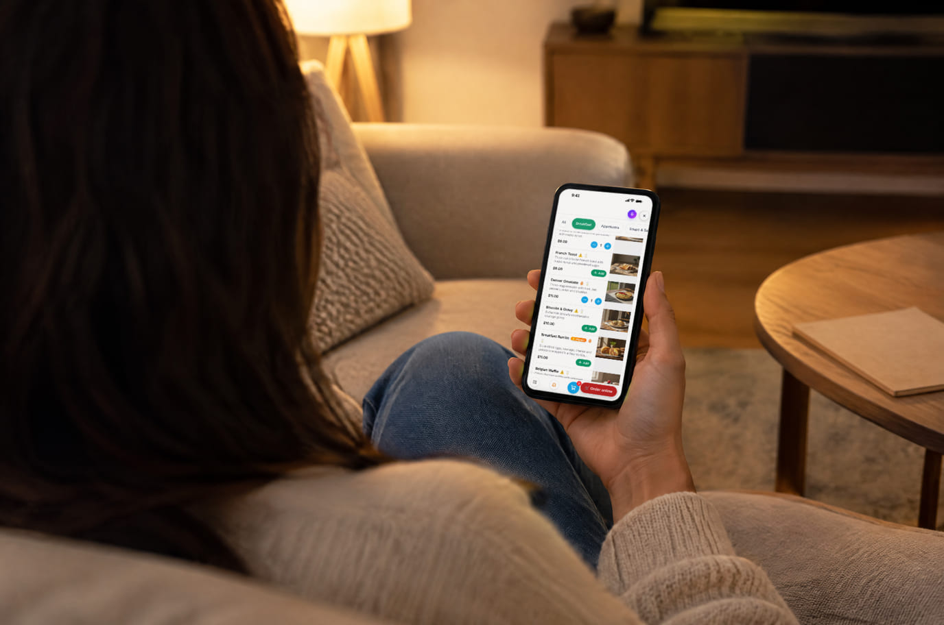 A guest on the sofa in the evening orders dinner from a restaurant website on her phone